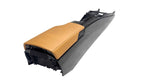 Load image into Gallery viewer, A custom car center console armrest featuring a tan leather seat cover and a black plastic housing, photographed on a light gray concrete floor.