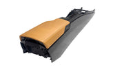 A custom car center console armrest featuring a tan leather seat cover and a black plastic housing, photographed on a light gray concrete floor.