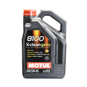 A quart of Motul 8100 X-Clean Gen2 5W-40 Synthetic Motor Oil with a black container and red cap, displayed on a wooden shelf.