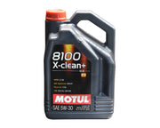 A quart bottle of Motul 8100 X-Clean+ 5W-30 Synthetic Motor Oil with a black body and orange cap, displayed on a table.